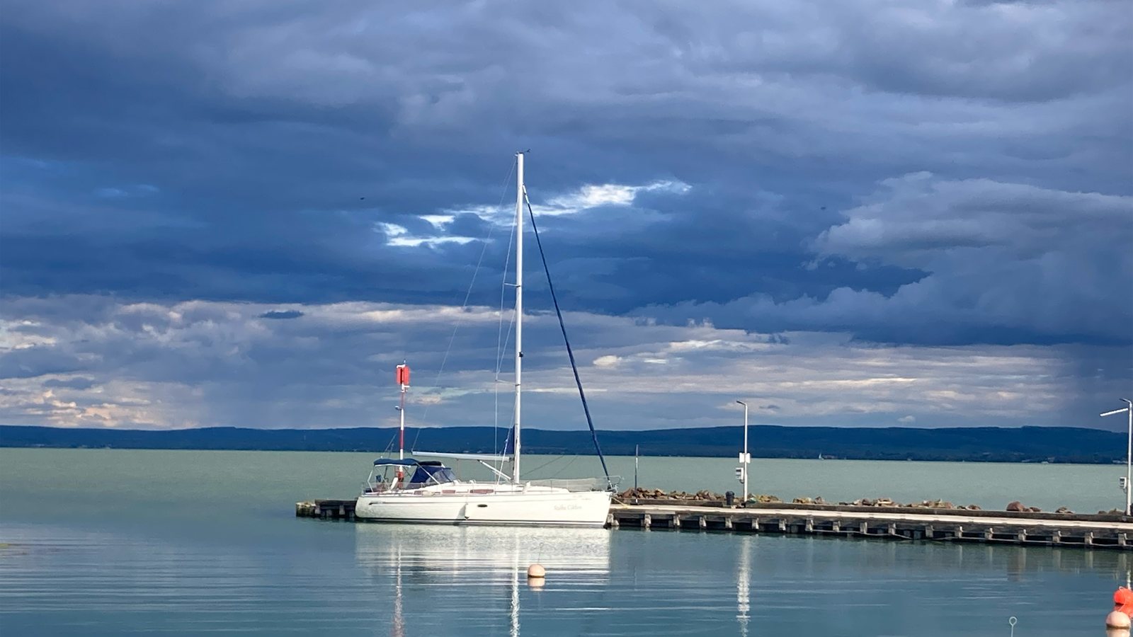 Szőke Ciklon moored on calm Lake Balaton beneath a dramatic sky